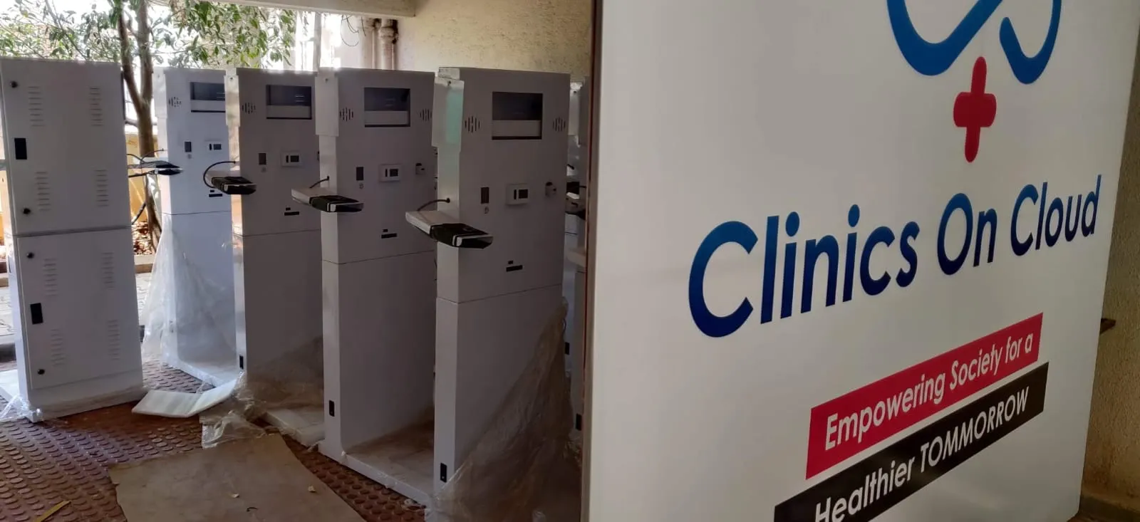 A batch of finished Clinics On Cloud health kiosks beside the company banner